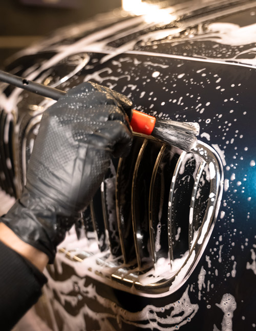 hand holding a brush cleaning a car grille with soap bubbles and water two step car wash cleaning process